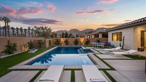 Un área de piscina moderna con vistas despejadas a las montañas al fondo, rodeada de palmeras y un césped bien cuidado.