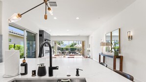 Una cocina moderna con una isla grande, pileta de acero inoxidable e iluminación colgante.