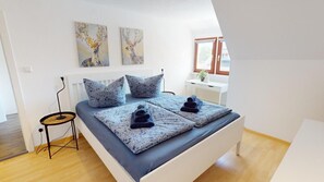 Ein modernes Schlafzimmer mit einem Bett, zwei an der Wand befestigten Bildern, einem Nachttisch und einem Fenster.