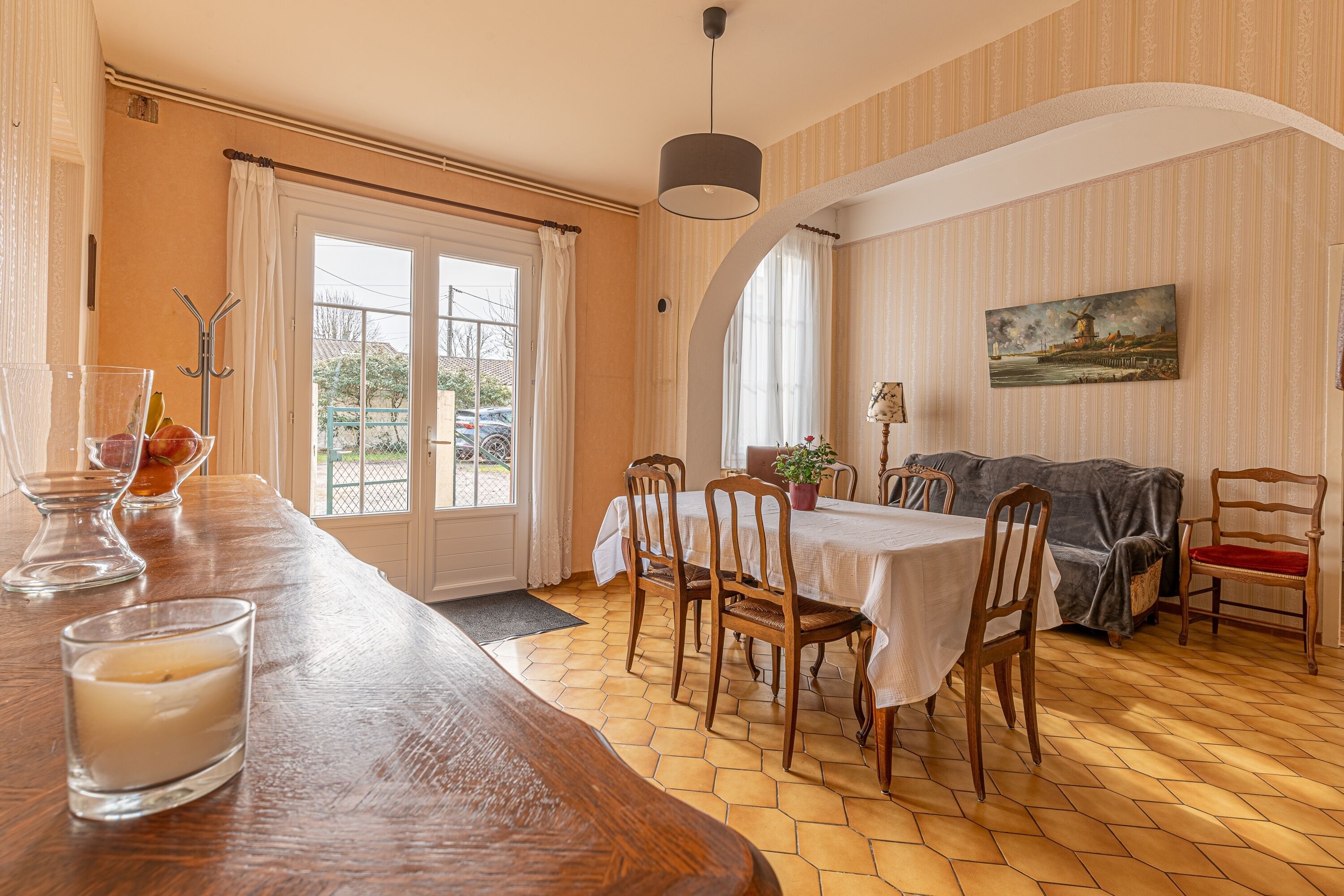 A dining area with a wooden table and chairs, a window with curtains, and a painting on the wall.