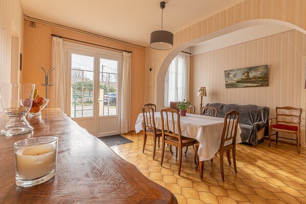 A dining area with a wooden table and chairs, a window with curtains, and a painting on the wall.
