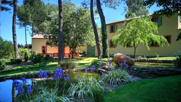 Un jardín con un estanque, árboles y un edificio de techo con tejas.