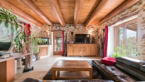 A rustic living room with a stone wall, wooden ceiling beams, a leather sofa, a coffee table, and a TV. - Villa Lorna - 2 maisons - piscine privée (Aups)