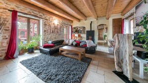 A cozy living room with a stone wall, wooden ceiling beams, a fireplace, and a large wooden table. - Villa Lorna - 2 maisons - piscine privée (Aups)