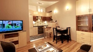 Un salon moderne doté d’un téléviseur à écran plat, d’un coin repas avec une table et des chaises, et d’une cuisine avec des meubles en bois et un four encastré.