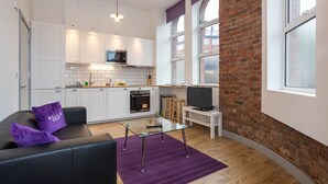 Een moderne keuken met witte kastjes, een bakstenen muur en een eetgedeelte met een glazen tafel.
