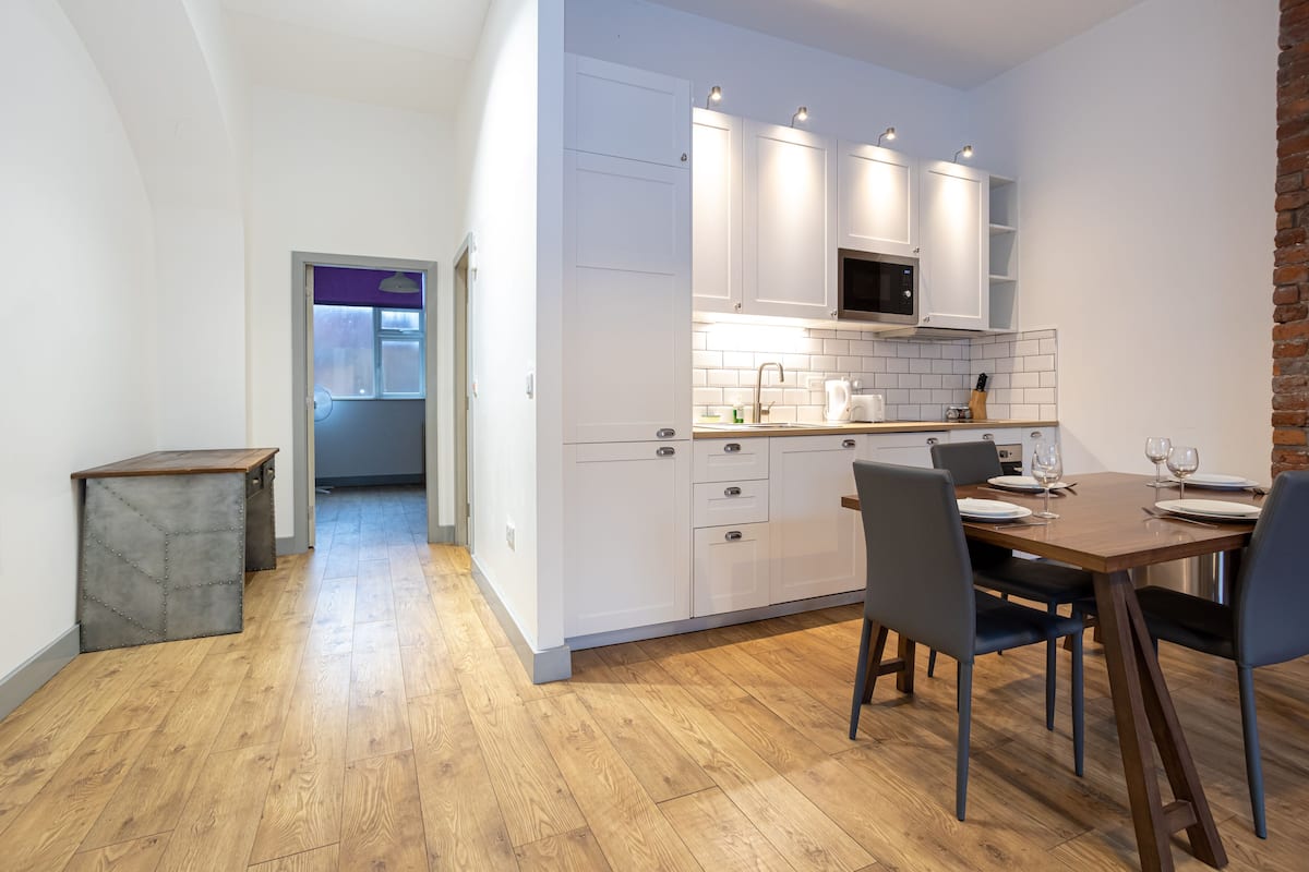 Una cocina moderna con armarios blancos, una mesa de comedor de madera y una pared de ladrillo decorativa.