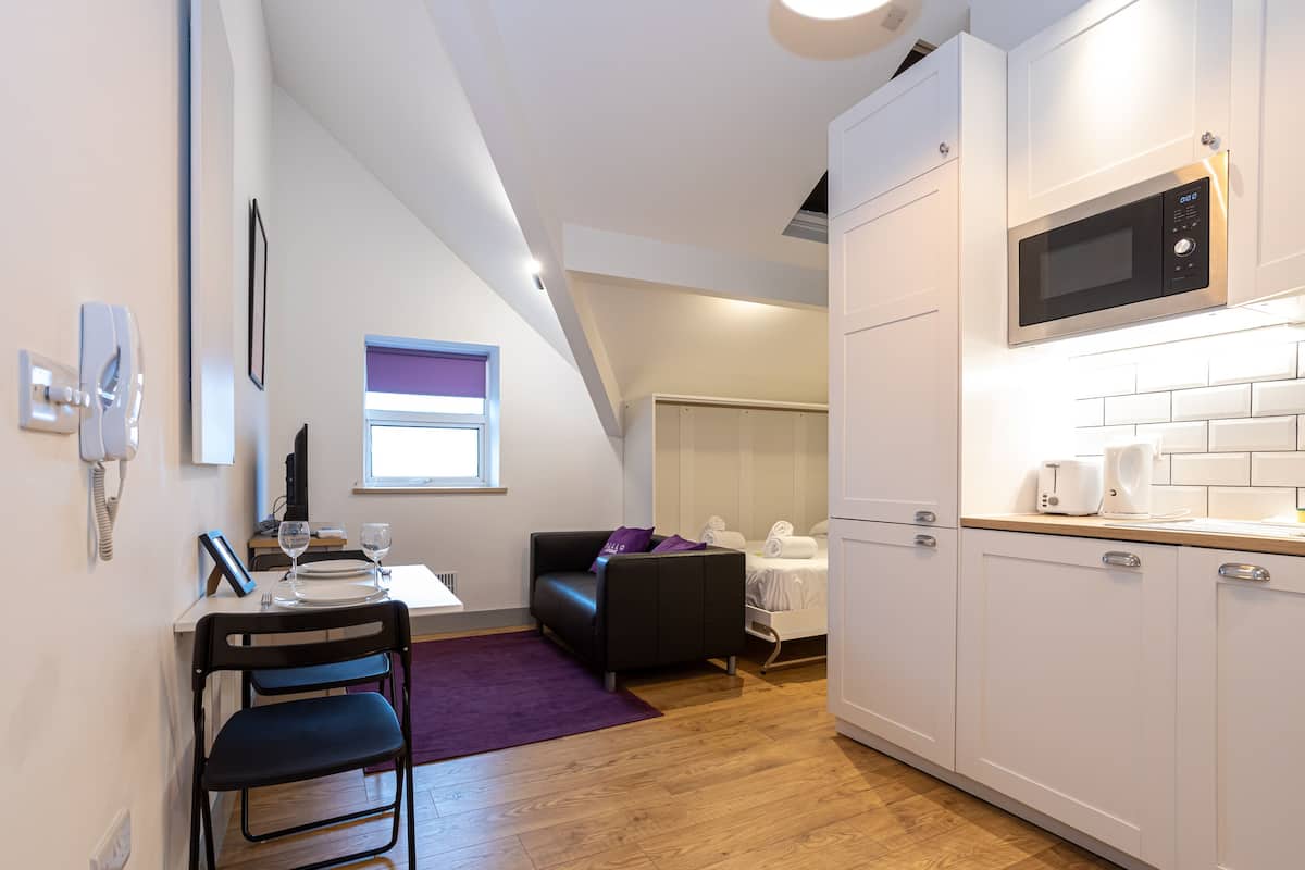 Una cocina compacta con muebles blancos, un microondas y un comedor con mesa y sillas.