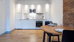 Een compacte keuken met witte kastjes, een magnetron en een metselwerk muur.