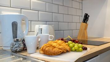 A kitchen counter with a cutting board, two croissants, a bunch of grapes, a coffee maker, and a knife block.