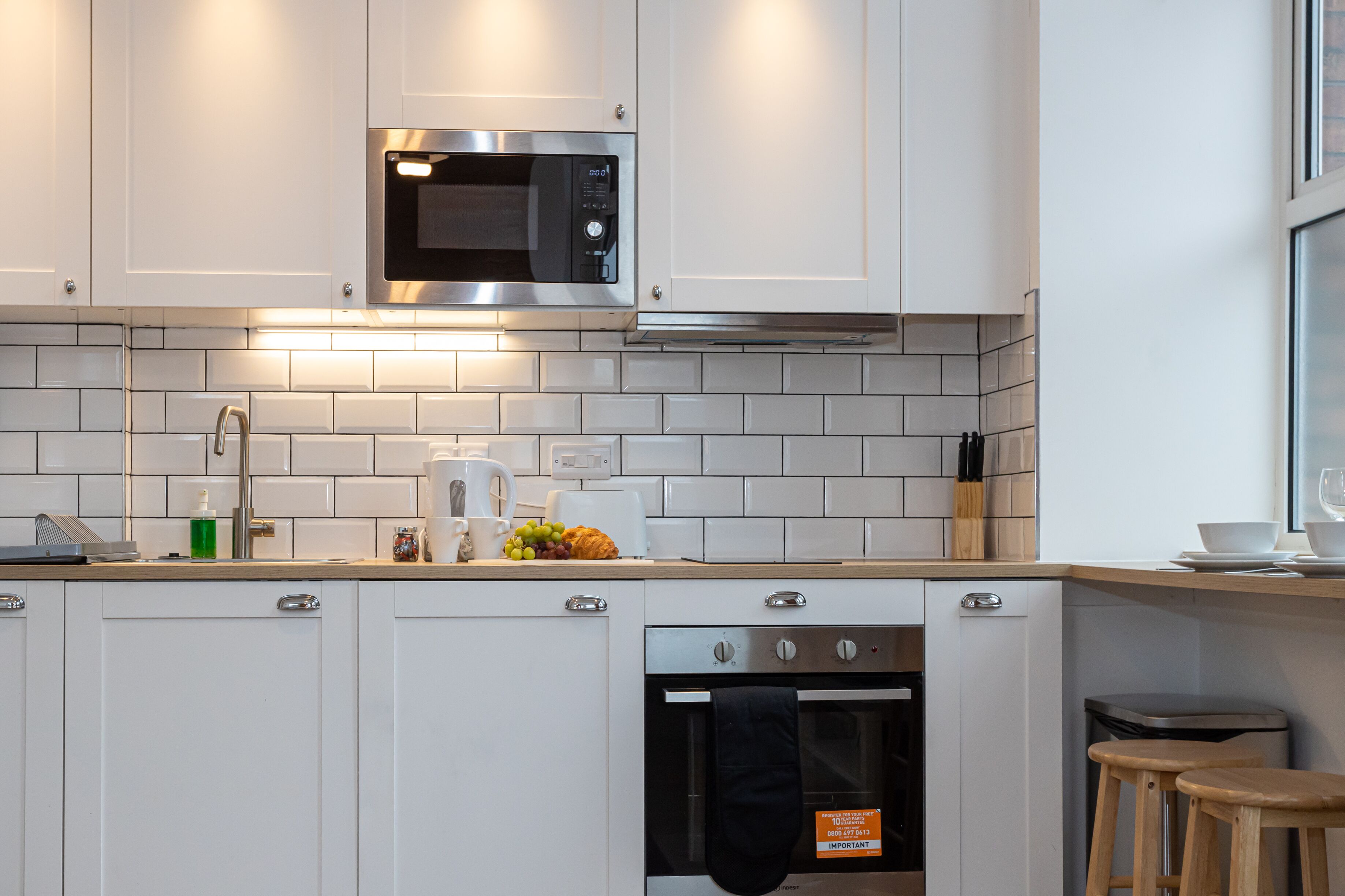 A modern kitchen with white cabinets, a stainless steel microwave, a built-in oven, and a tiled backsplash.
