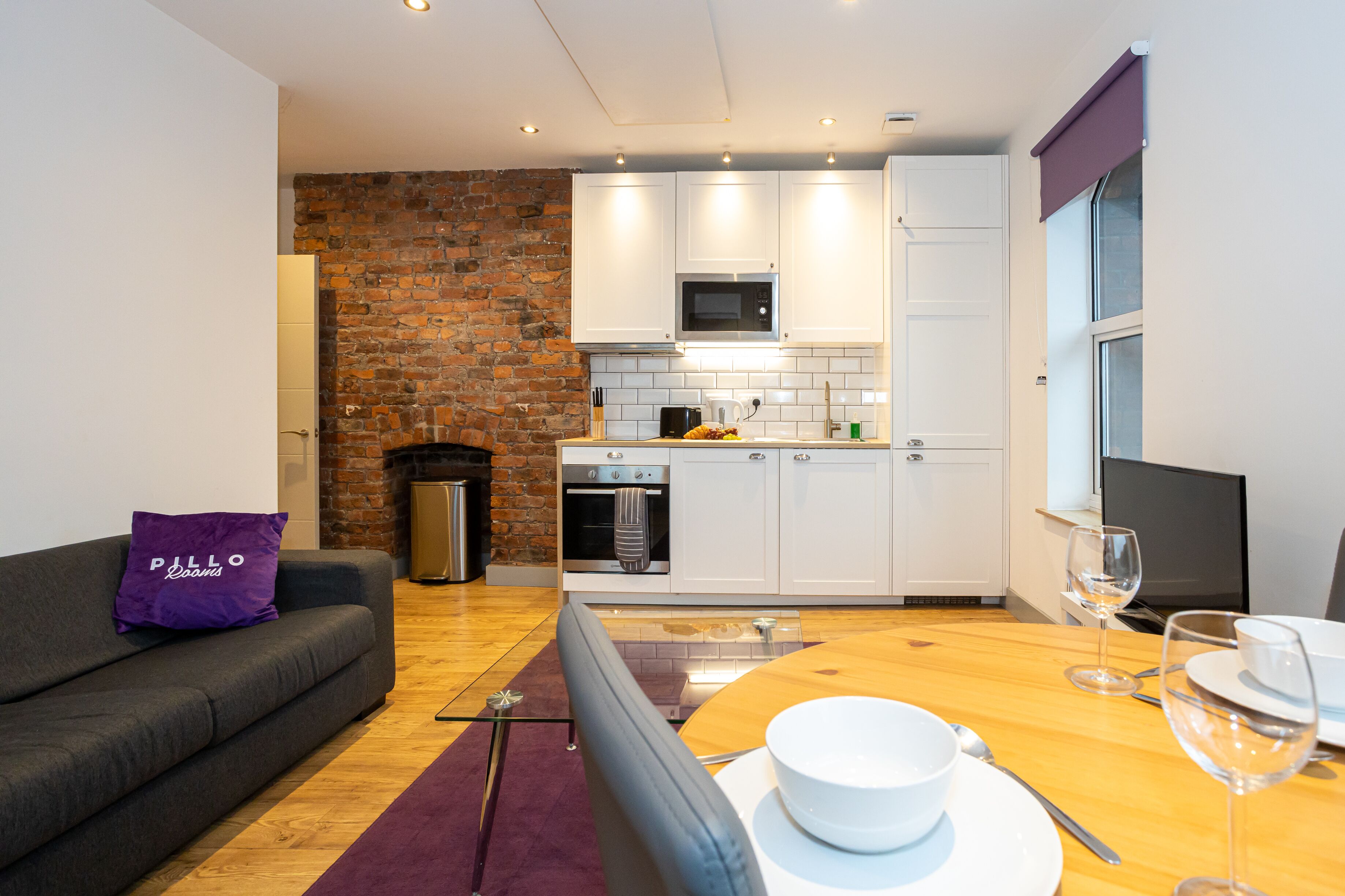 Una cocina moderna con armarios blancos, una pared de ladrillo y un comedor con una mesa dispuesta para dos.