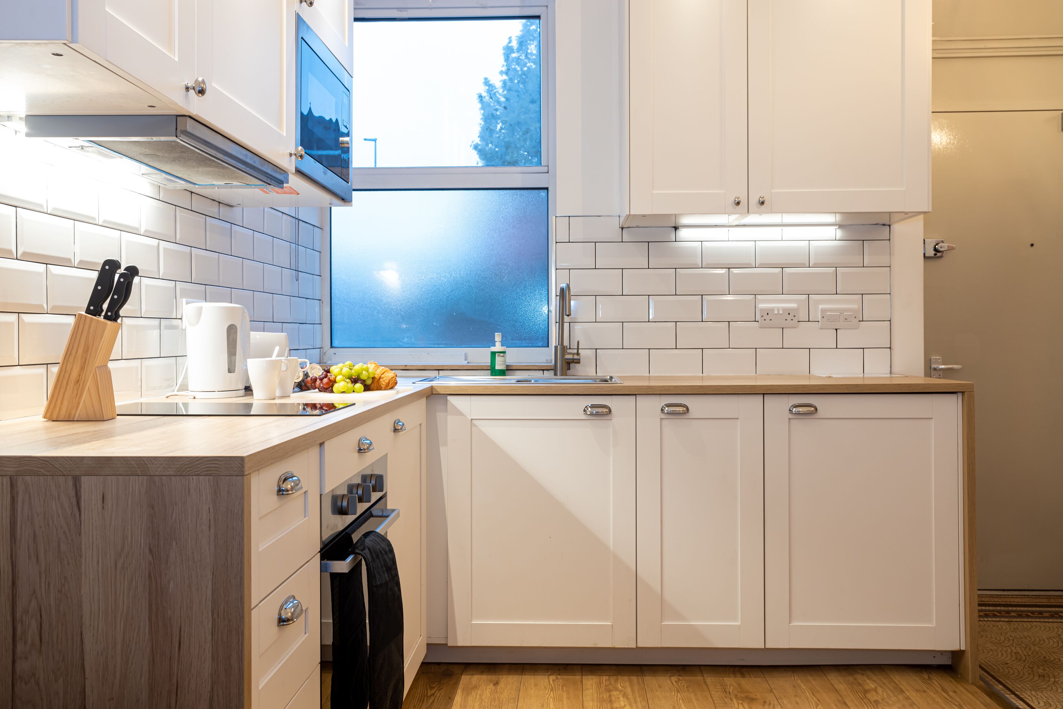 Una cocina moderna con armarios blancos, encimera de madera y ventana con vistas a árboles.