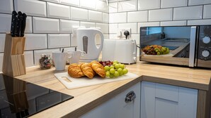 Een moderne keuken met witte tegels, een zwarte inductiekookplaat, een broodrooster en een snijplank met croissants en druiven.