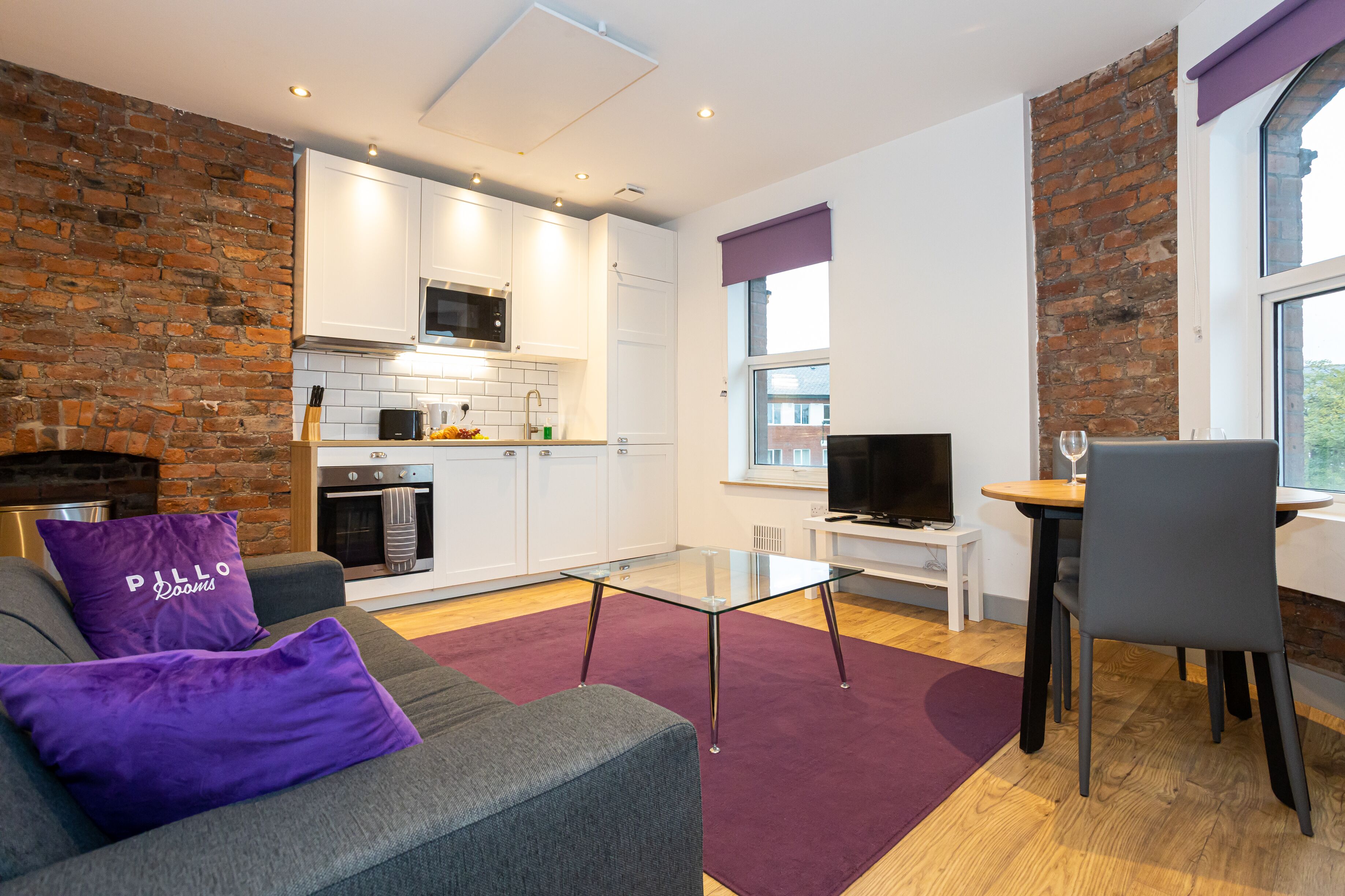 A modern living room with a sofa, a glass coffee table, and a dining area with a TV and table.