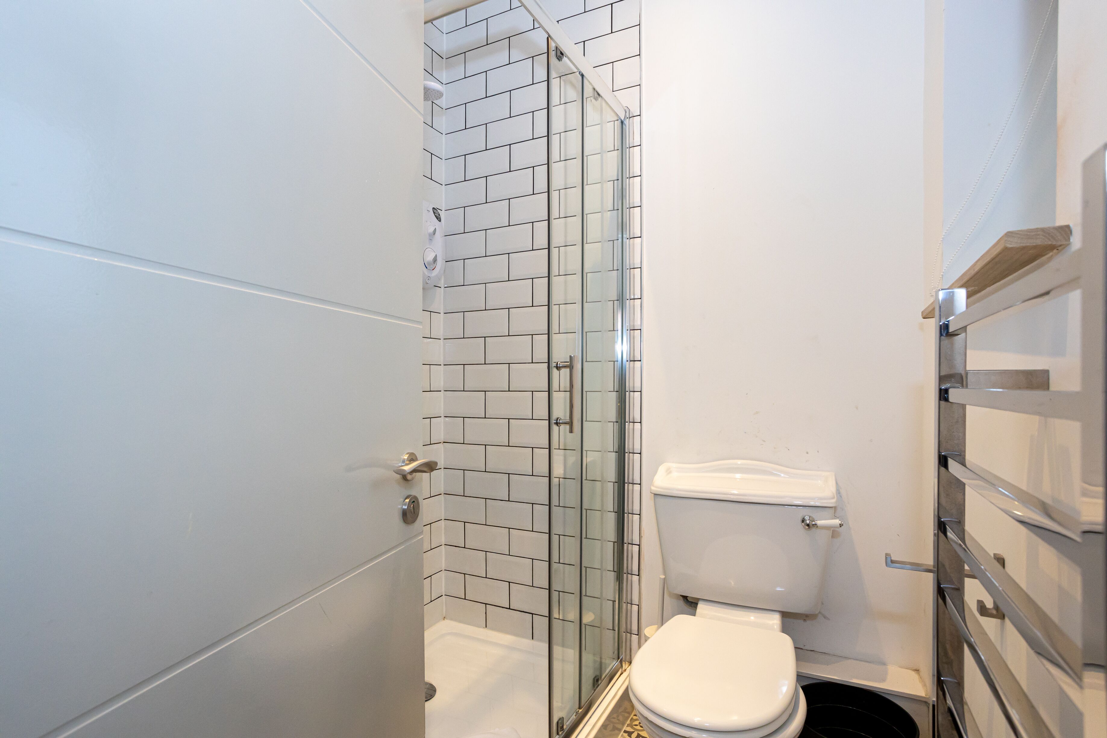 Une petite salle de bain dotée d’une douche à parois de verre, de toilettes blanches et d’un mur carrelé.