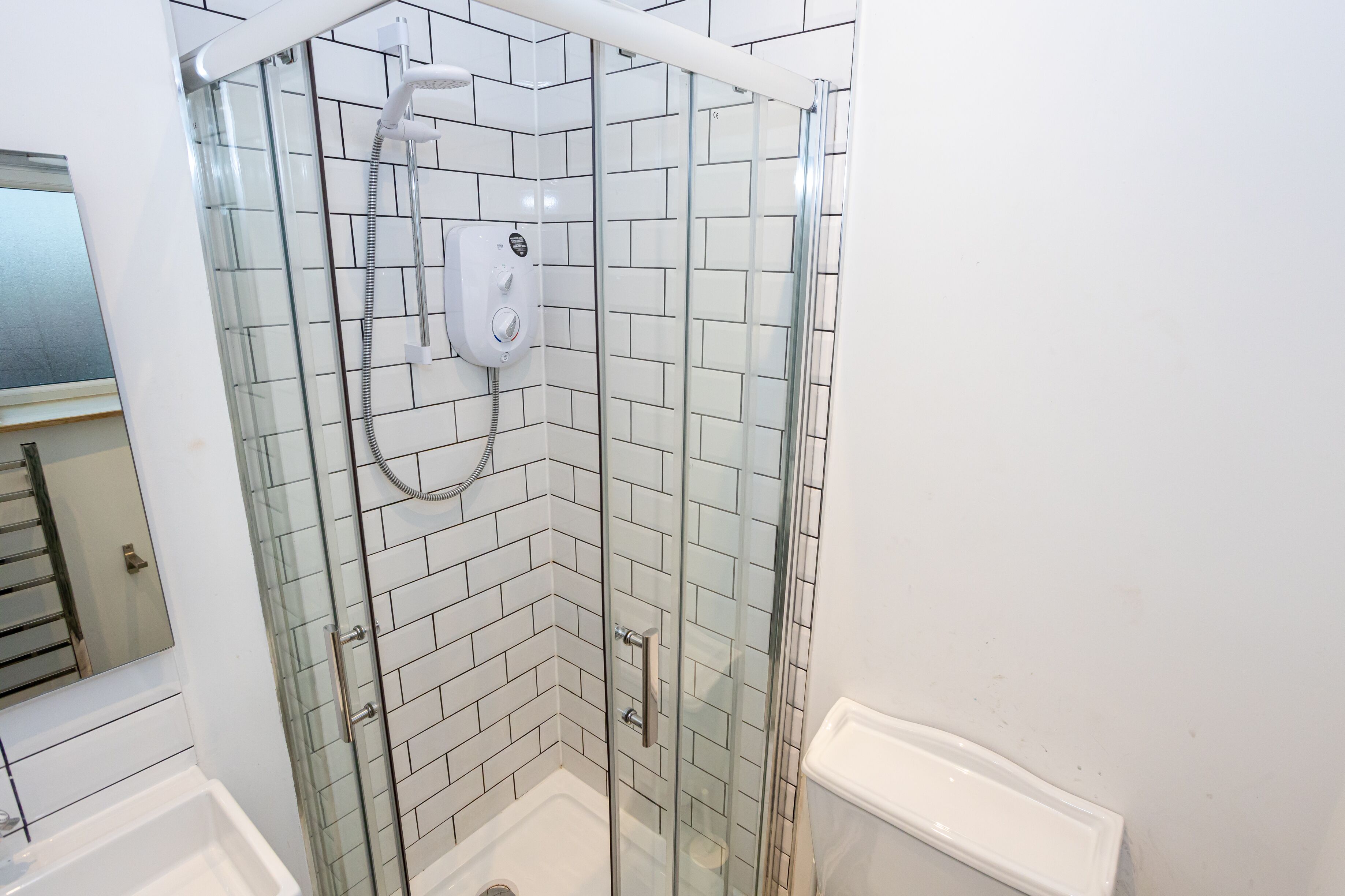 A glass-enclosed shower with a handheld showerhead and a wall-mounted control panel.