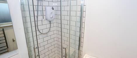 A glass-enclosed shower with a handheld showerhead and a wall-mounted control panel.