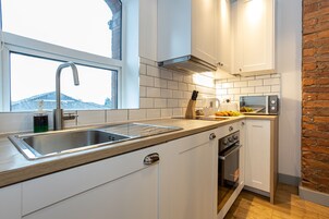 Una cocina moderna con armarios blancos, un lavamanos de acero inoxidable, horno empotrado y una pared decorativa de ladrillo.