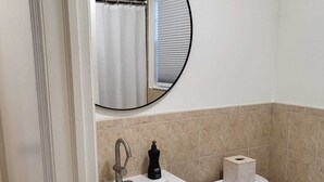 A bathroom with a white sink, a mirror, a toilet, and beige tiled walls. - Upscale & Elevated - 3BR 2BA (Newark)