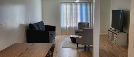 Una sala de estar moderna con una mesa de comedor de madera, un sofá, una mesa de centro y un televisor.