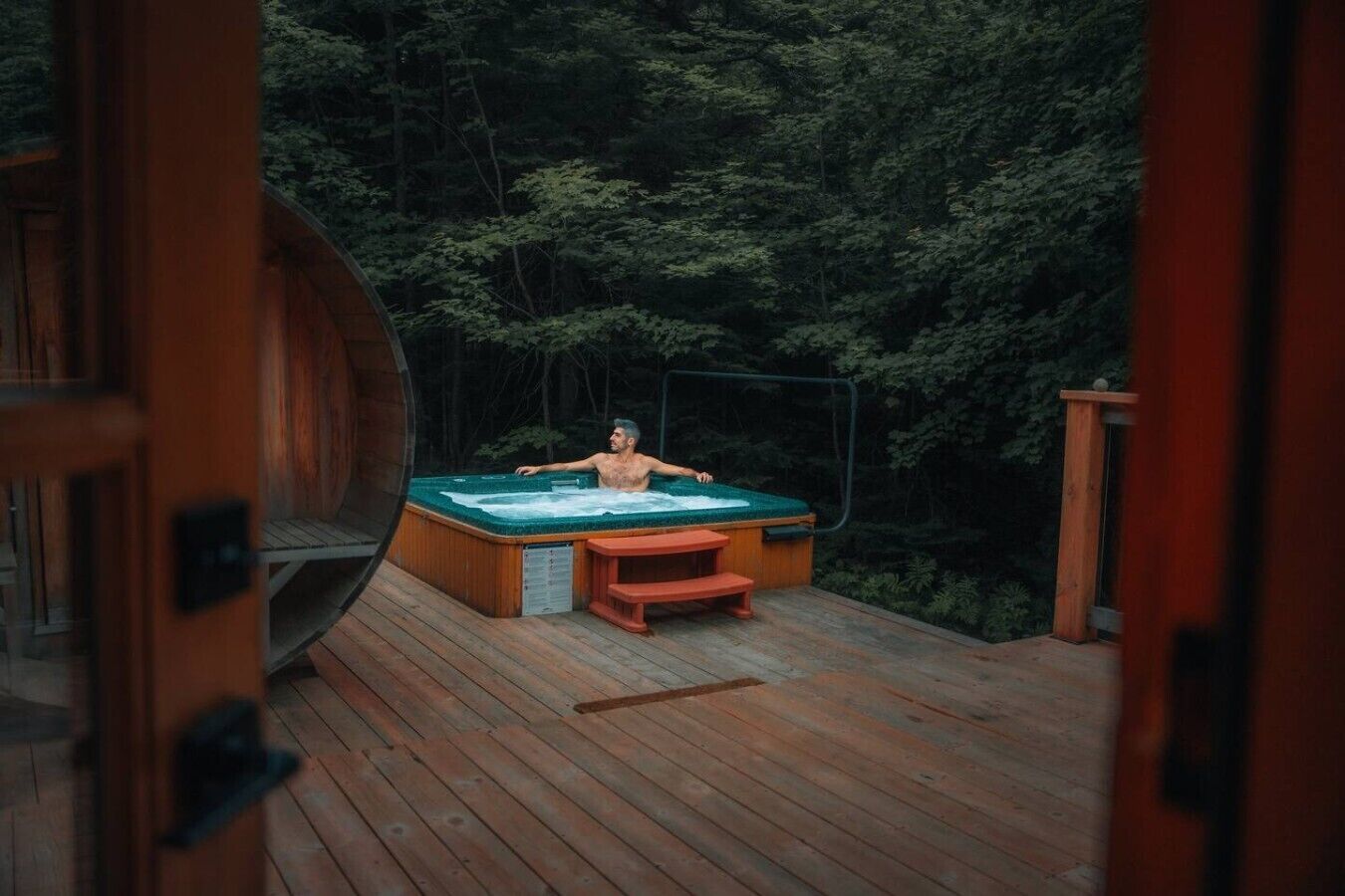 Une terrasse en bois avec un jacuzzi et une table, entourée d’une forêt dense.