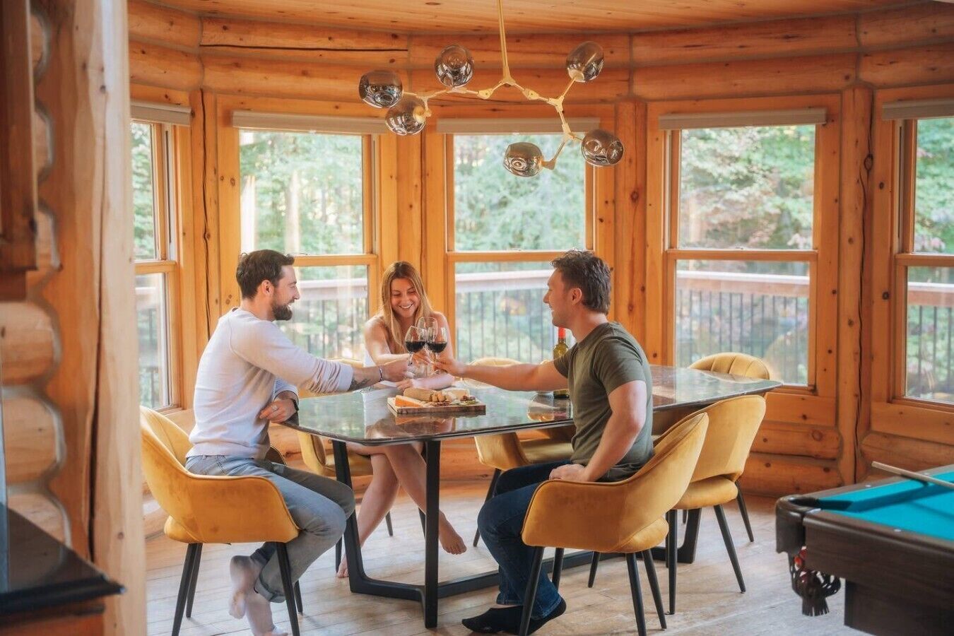 L’intérieur d’un chalet en bois comprend une table à manger, des chaises et une table de billard.