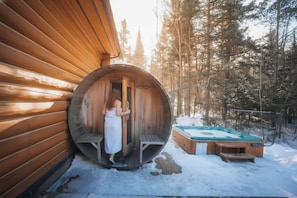 Une cabane en bois dotée d’un sauna, d’un bain à remous et surplombant une forêt enneigée.
