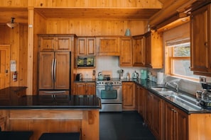 Une cuisine de style rustique, avec des éléments en bois, un îlot central, des appareils électroménagers intégrés et une fenêtre qui laisse entrer la lumière naturelle.