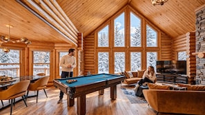 Ein rustikales Holzblockhaus-Interieur mit Billardtisch, einer Couch und einem Fernseher.