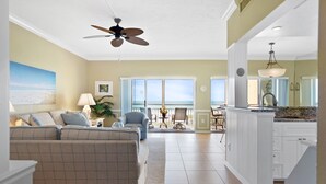A spacious living room with a large sofa, a dining area with chairs, a kitchen with white cabinets, and a ceiling fan. - Anna Maria Island Direct Beachfront Condo- Awesome View and Amazing Sunsets (Holmes Beach)