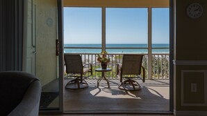 A balcony with two rocking chairs and a small table with a plant, overlooking a beach. - Anna Maria Island Direct Beachfront Condo- Awesome View and Amazing Sunsets (Holmes Beach)