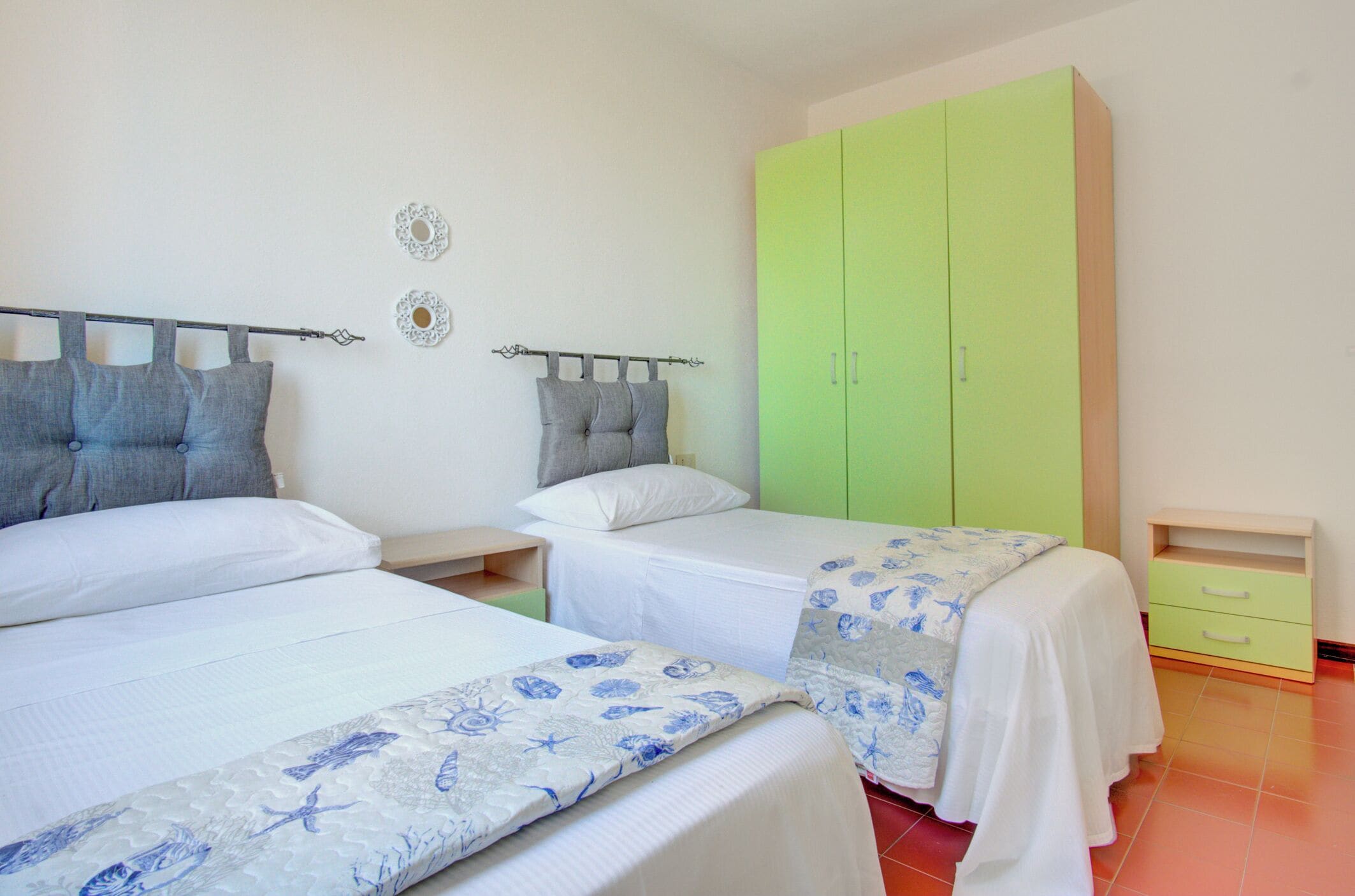 Een slaapkamer met twee bedden, een groene garderobe en een klein nachtkastje.
