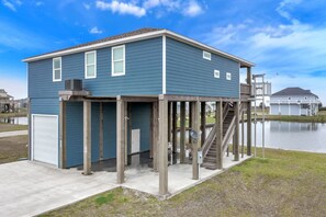 A two-story house with a dock extending into a body of water, a garage, and a staircase leading to the upper floor. - Born To Beach - Beach view, cargo lift, 4 bedrooms, Sleeps 12 (Crystal Beach)
