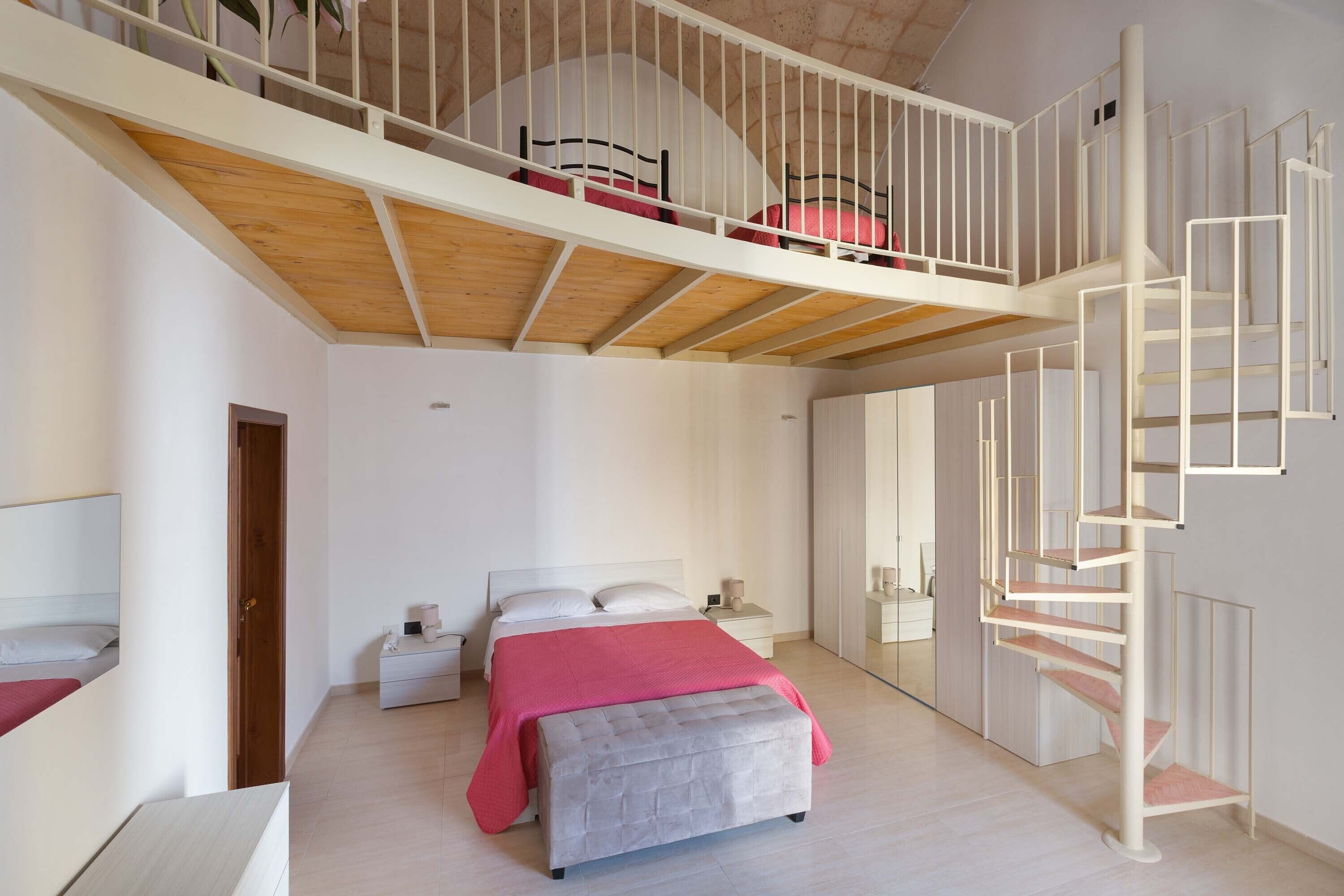 A modern bedroom with a lofted sleeping area, a large bed, a bench, and a spiral staircase.