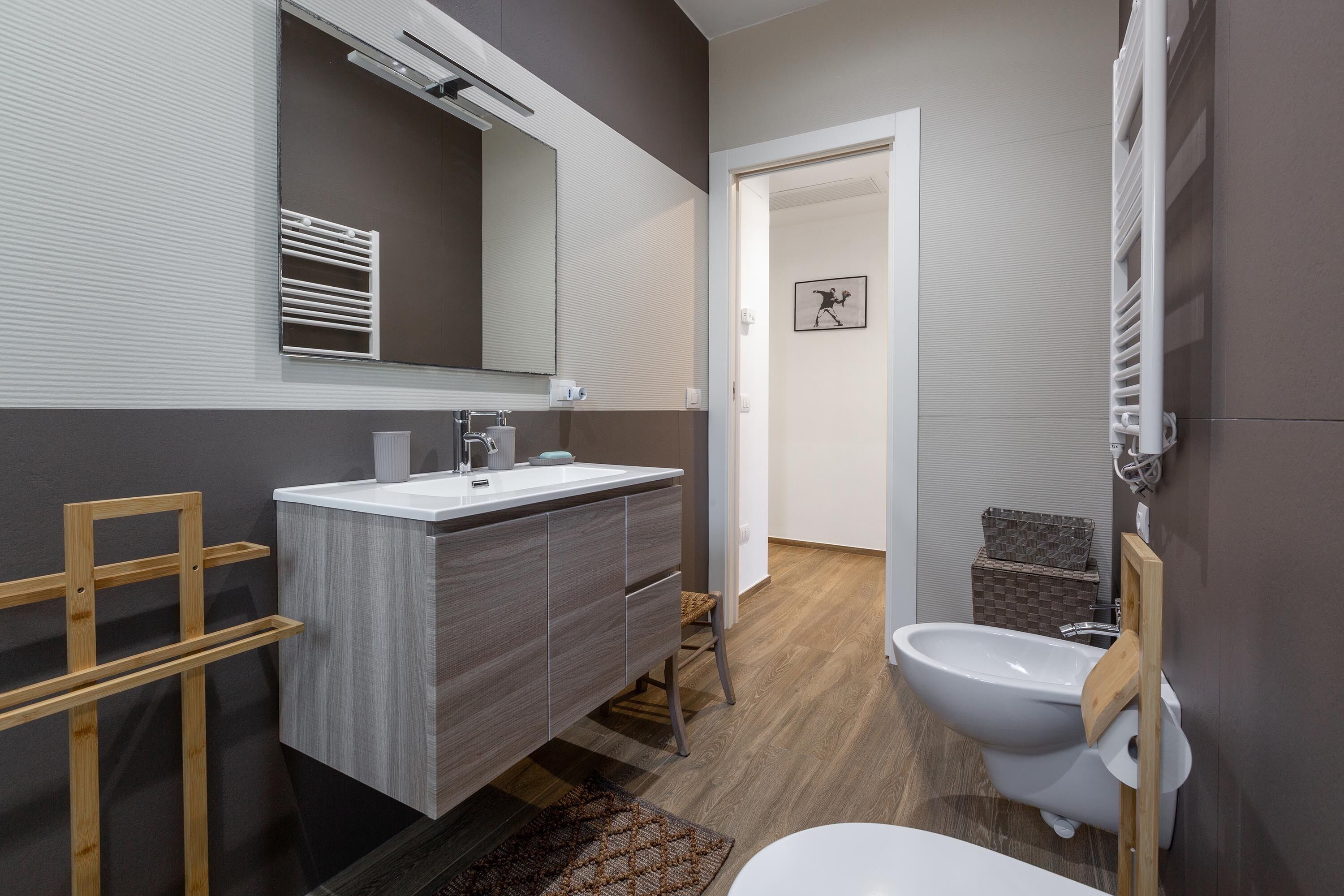 A modern bathroom with a wooden vanity, a large mirror, a bidet, and a shower area.
