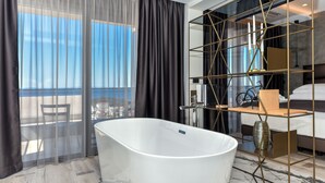 Un baño moderno con una bañera independiente, cabina de ducha de vidrio y vistas de la ciudad a través de cortinas traslúcidas.