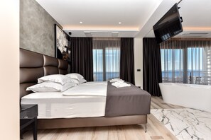 Een moderne hotelkamer met een groot bed, een flatscreen televisie, een badkuip en uitzicht over de stad.