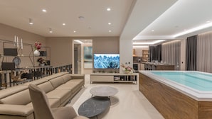 Una sala de estar moderna con un sofá color beige, una mesa de centro redonda, un televisor y un área de piscina.