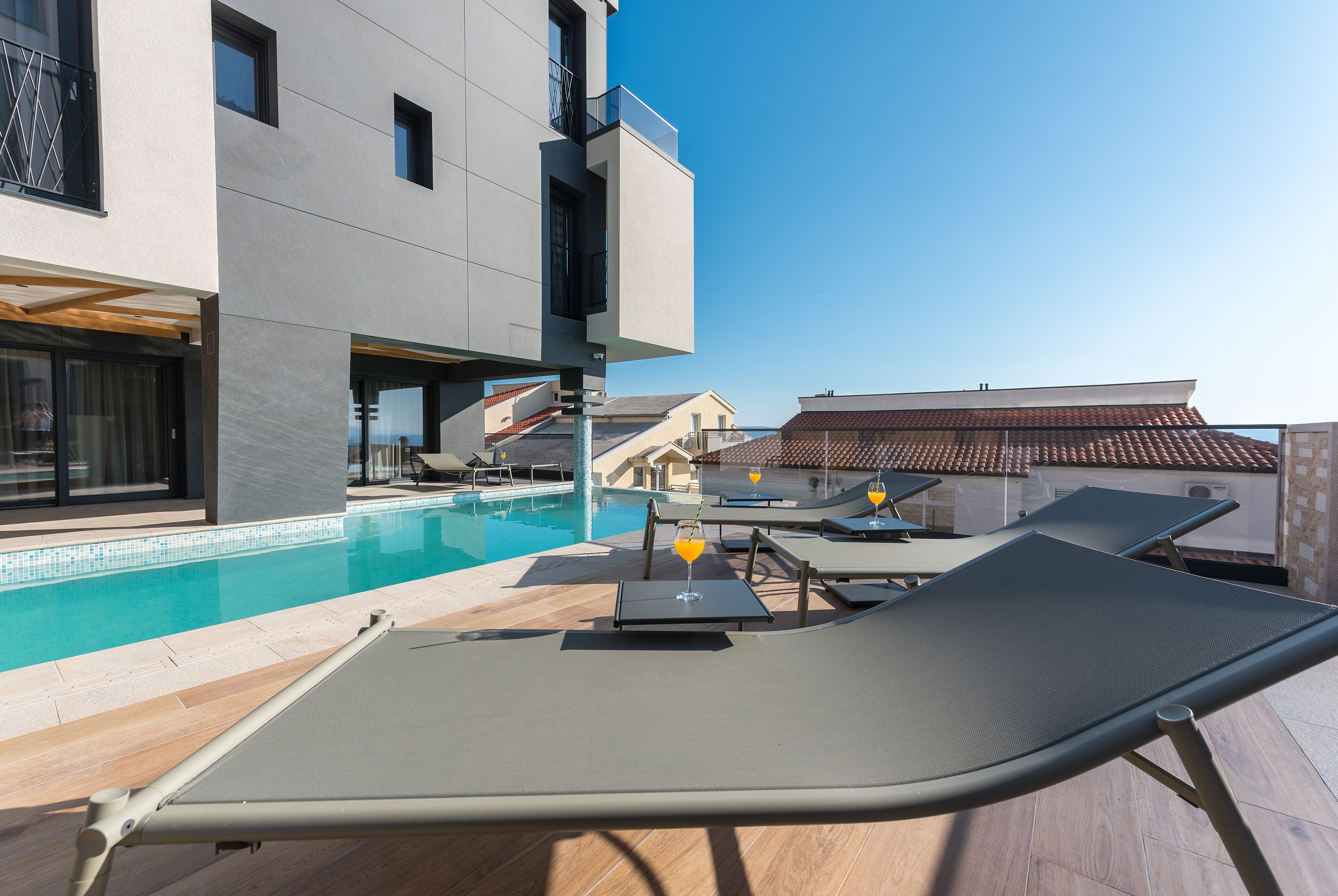 A modern poolside area with lounge chairs, a swimming pool, and a building with balconies.