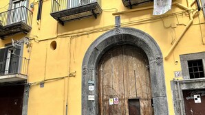 A building with a large arched wooden door, numbered 154, and a small balcony above it. - A Room de Scugnizzi (Naples)