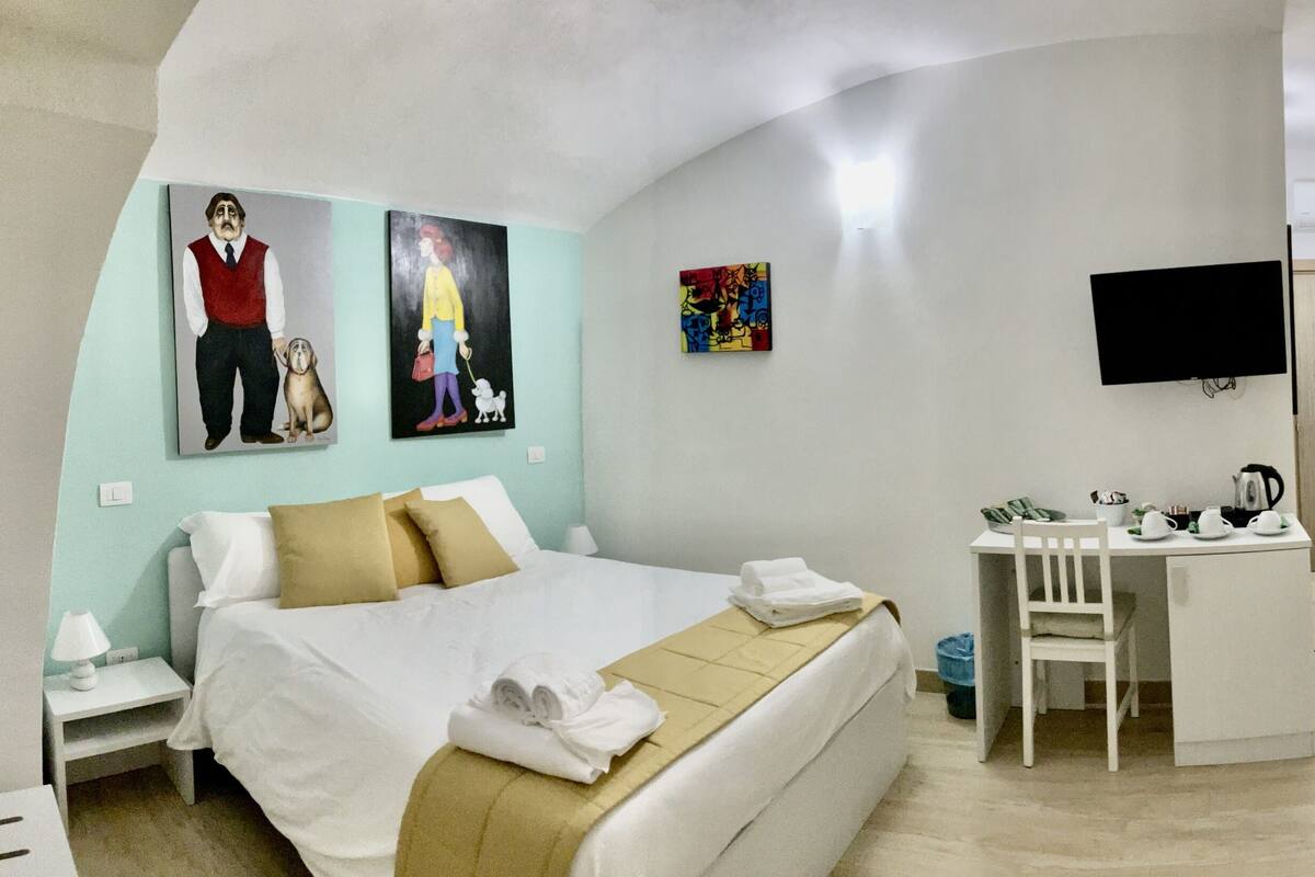 A hotel room with a bed, desk, chair, and artwork on the walls.