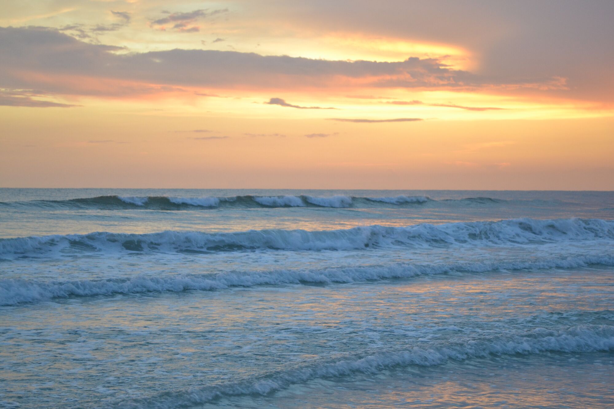 A beach with waves and a sunset.