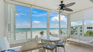 Ein Balkon mit Blick auf den Strand, einem runden Tisch und Stühlen mit gemusterten Kissen.