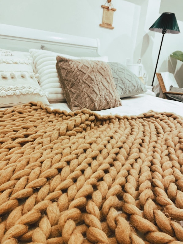 A bed with a brown knitted blanket, white pillows, and a bedside lamp.