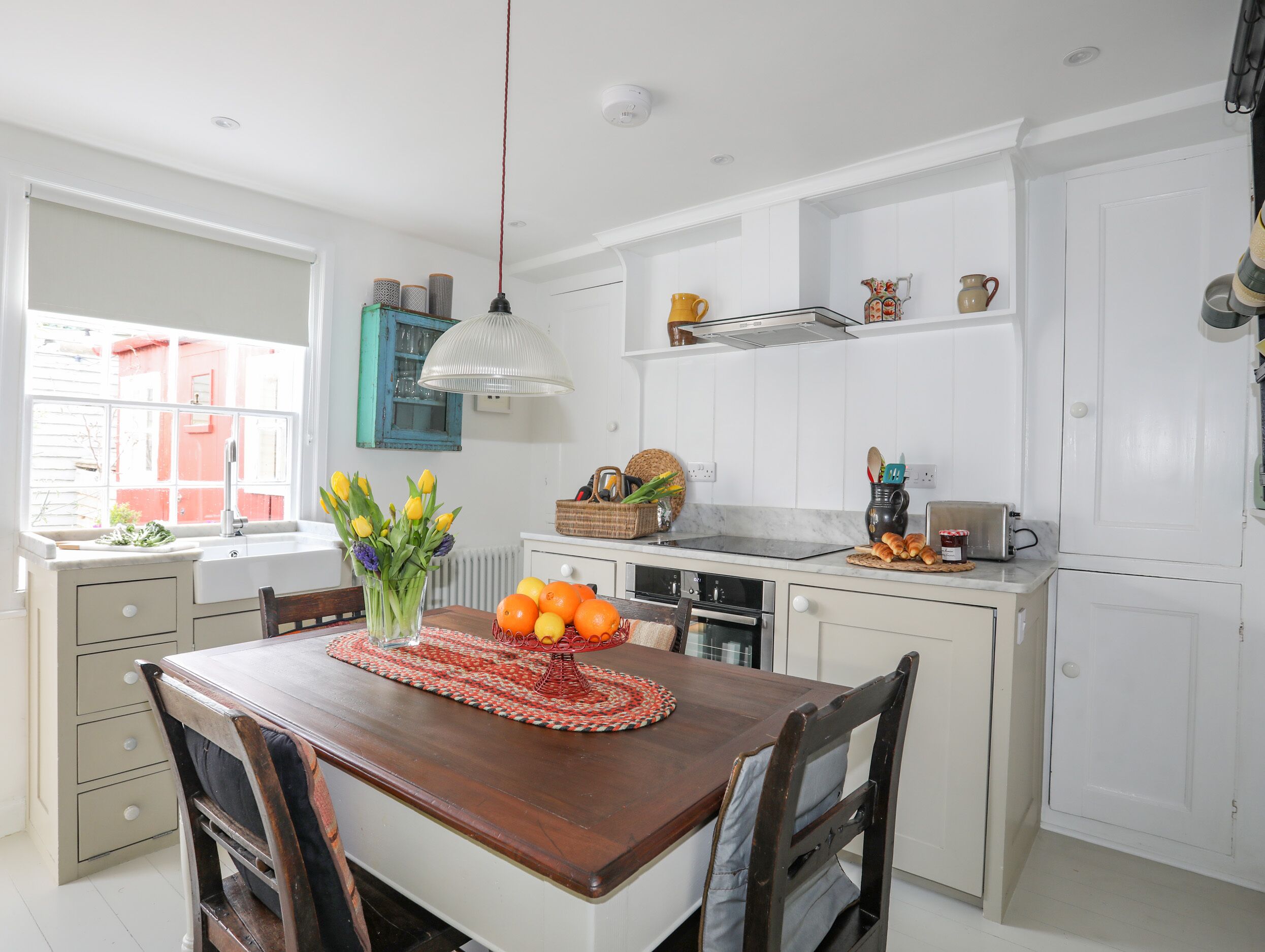 A kitchen with a wooden table, white cabinets, and a window with a view of a red building.