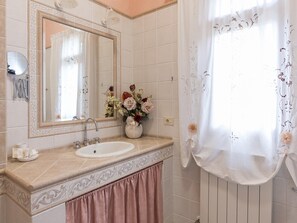 Une salle de bain avec un grand miroir, un lavabo et un vase de fleurs.