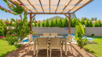 A covered outdoor dining area with a pool in the background.