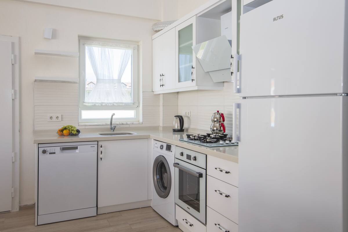 A modern kitchen with a dishwasher, washing machine, oven, and a refrigerator.