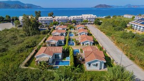 Zona residencial costera con villas que tienen piscinas, una calle pavimentada y vistas al mar.